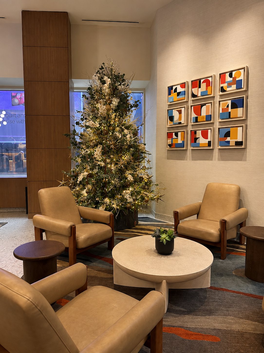 Hotel lounge Christmas tree beside leather armchairs and a coffee table, styled by Light the Lights
