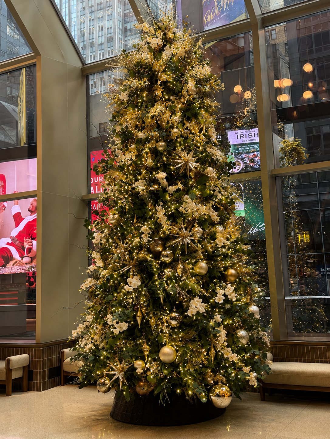Gold and white Christmas tree in a lobby with floor-to-ceiling city view windows, styled by Light the Lights