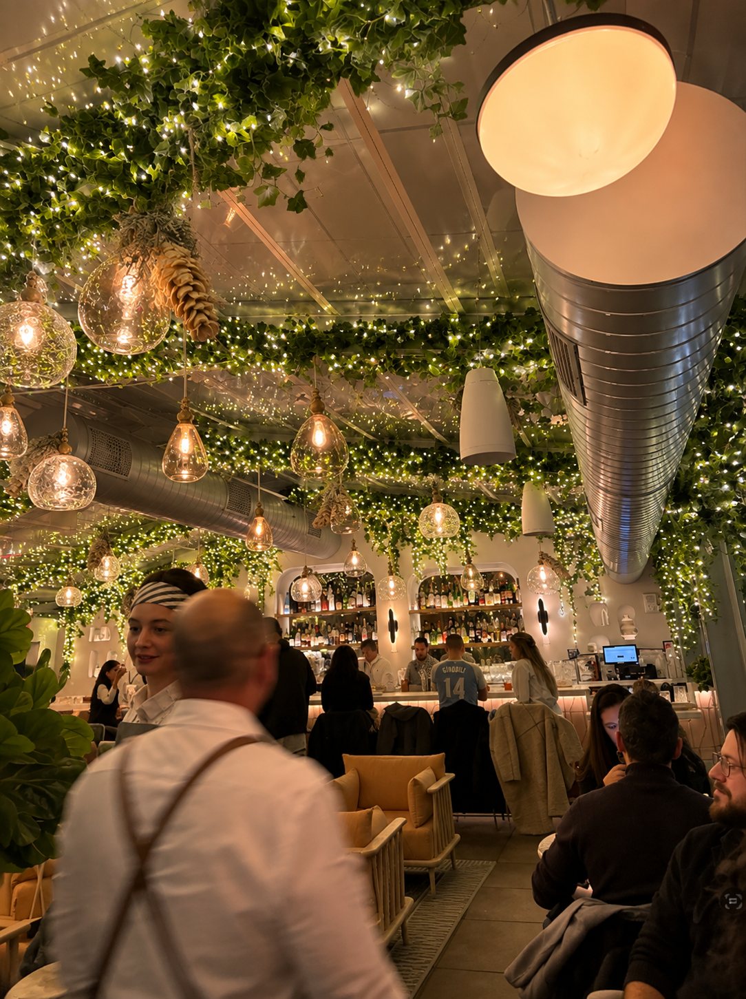 Restaurant ceiling wrapped in hanging greenery and string lights over the bar, styled by Light the Lights