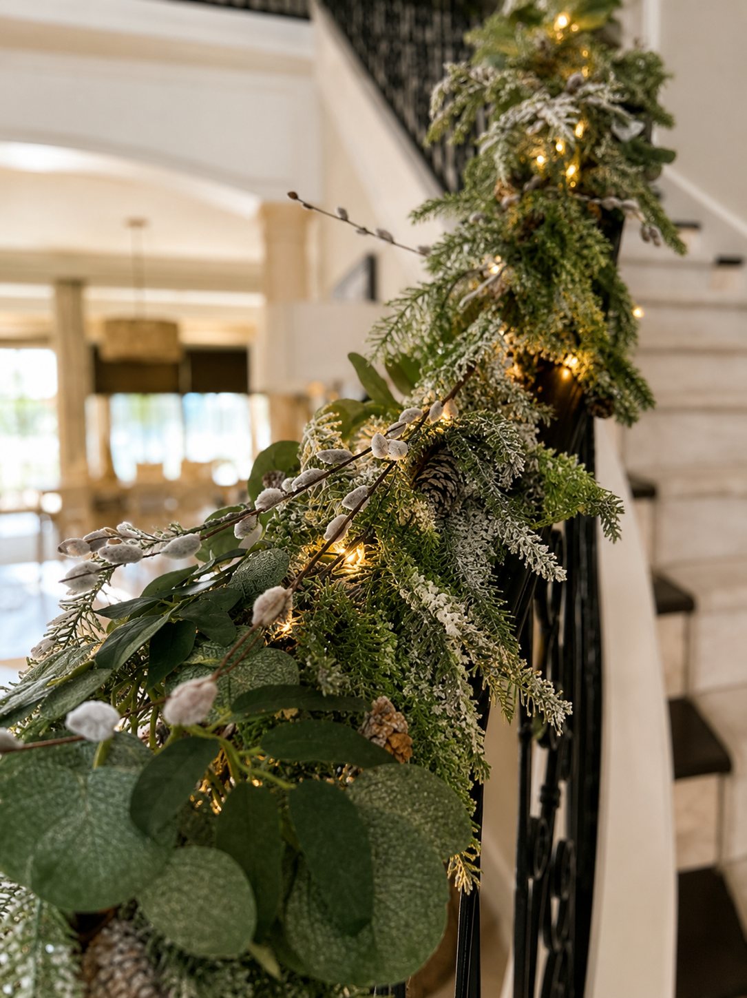 Staircase railing wrapped in garland, pinecones, and string lights, styled by Light the Lights