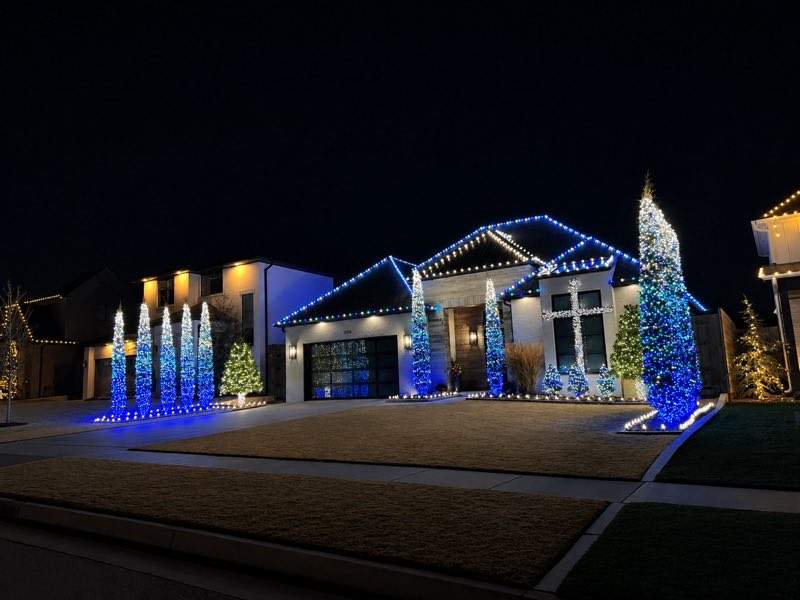 Home decorated in blue and white holiday lights with lit cone trees