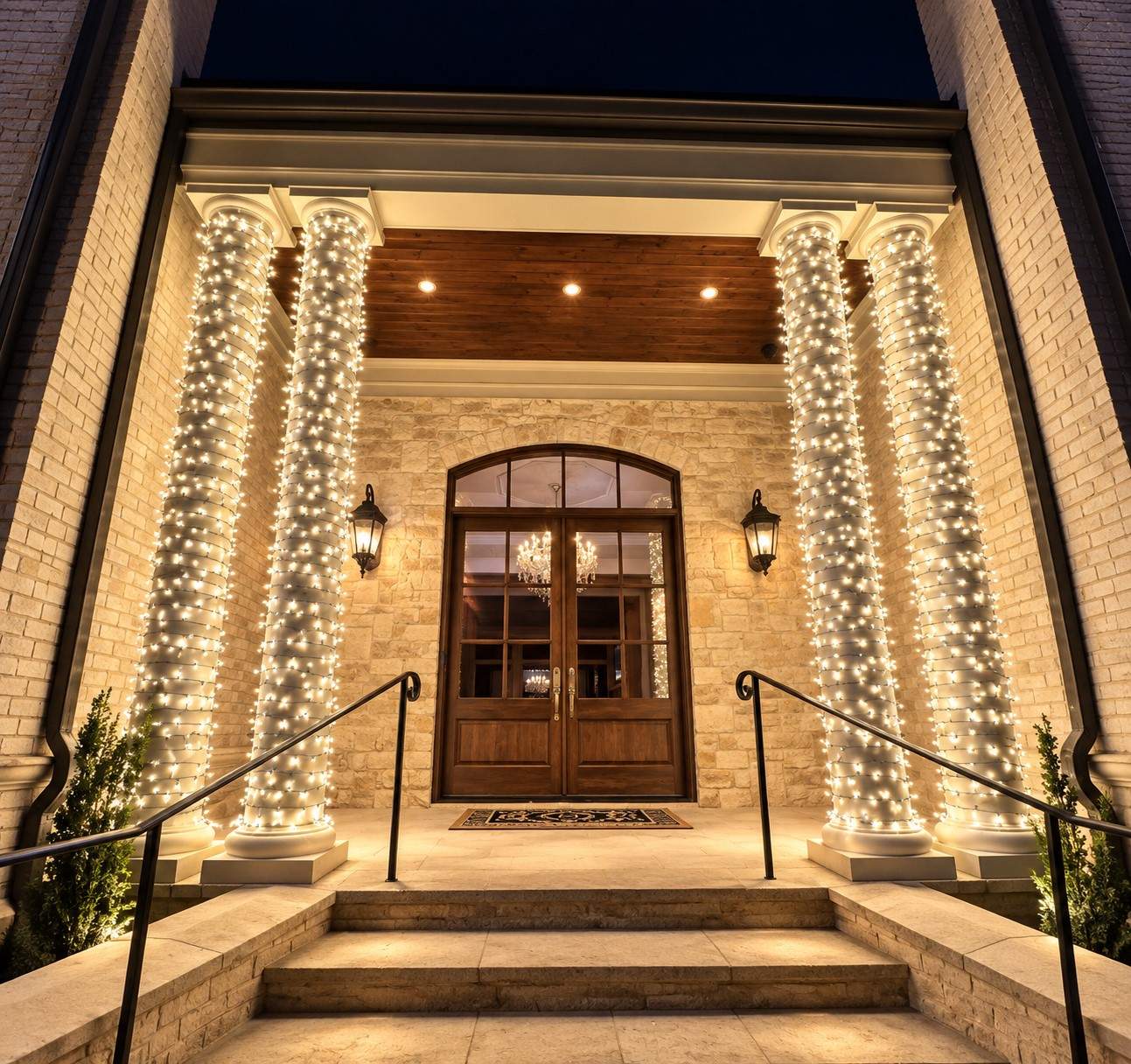 Columns wrapped in warm white lights at a home entrance
